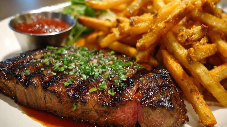 A slab of steak with French fries and a cup of ketchup beside it