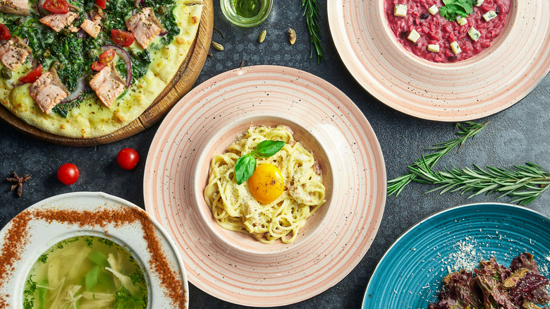Assorted Italian foods including pizza with pesto, pasta with an egg yolk, and beetroot risotto