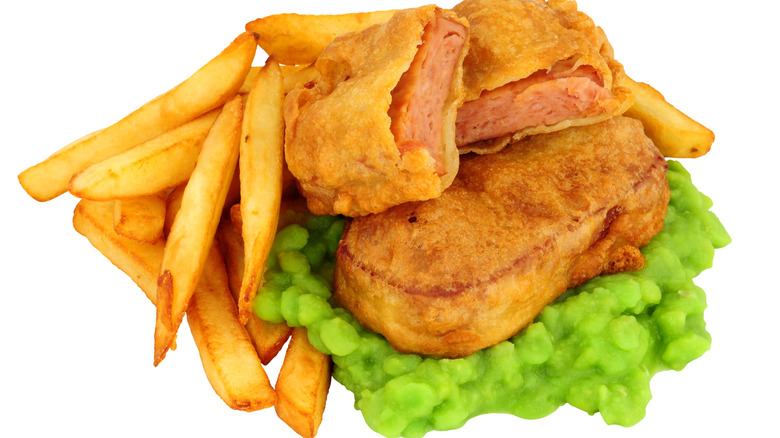 Spam fritters on top of mushy peas and next to french fries on white background