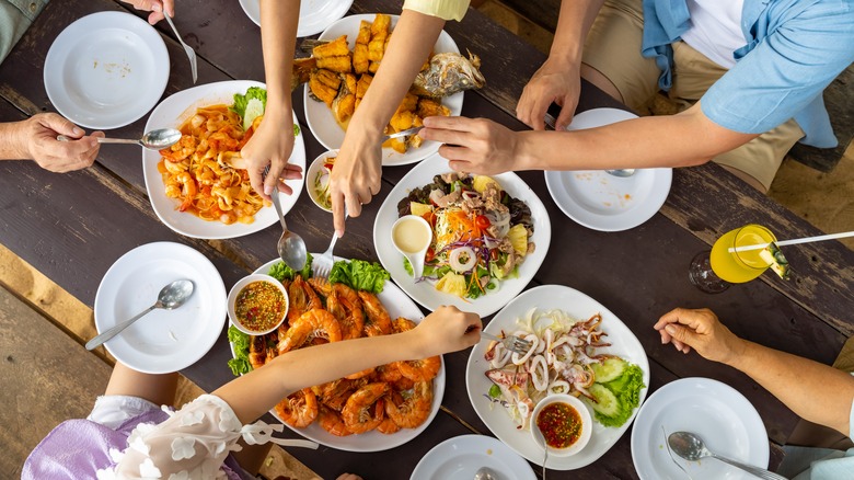 People serving themselves at table with various seafood dishes