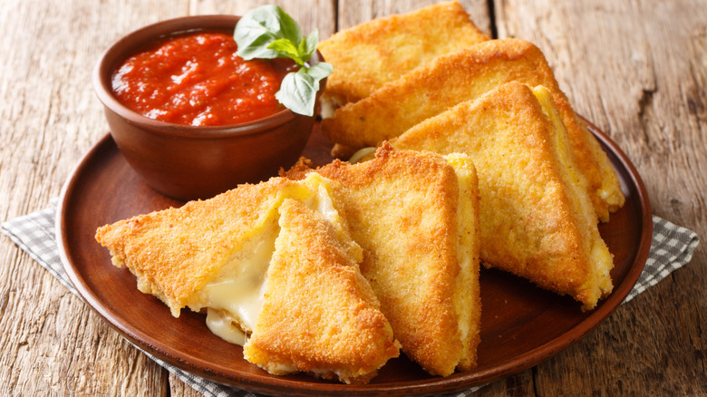 Mozzarella in carrozza sandwich triangles with a cup of marinara sauce.