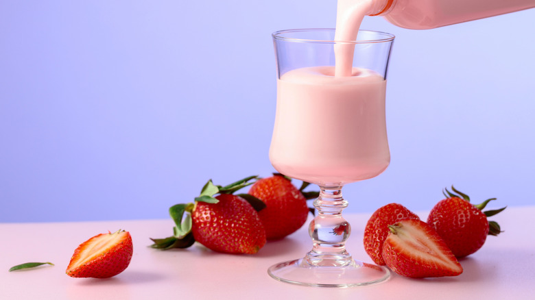A strawberry smoothie being poured into a glass beside fresh strawberries