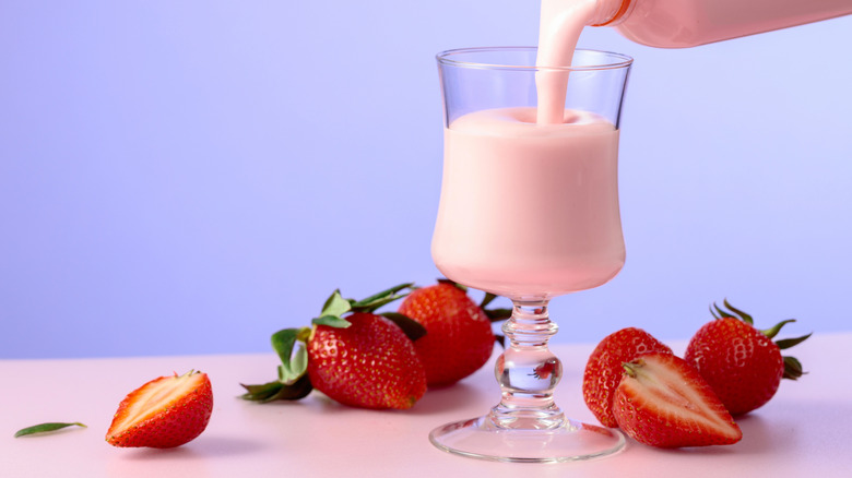 A strawberry smoothie being poured into a glass beside fresh strawberries