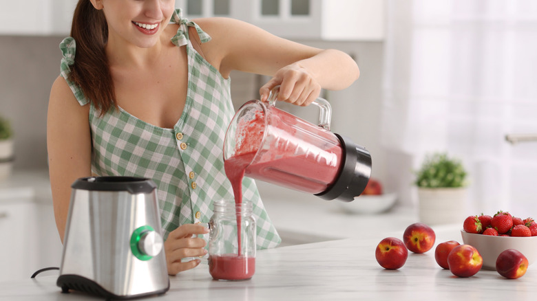 A woman pouring a red smoothie from a blender into a large jar