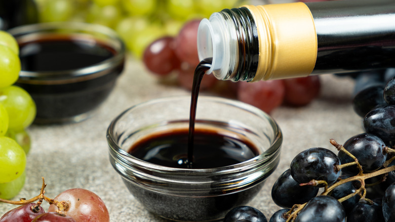 Balsamic vinegar being poured out of a bottle into a glass ramekin.