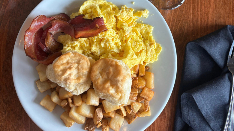 Plate with scrambled eggs, biscuits, home fries, and bacon