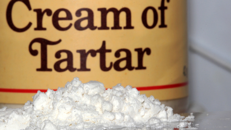 A closeup of a cream of tartar container with a pile of cream of tartar powder in front