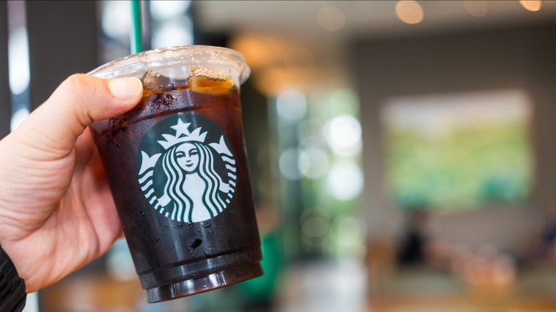 hand holding up black iced coffee from Starbucks inside store