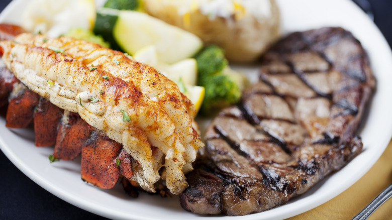 A plate of surf and turf with steak, a lobster tail, and veggies
