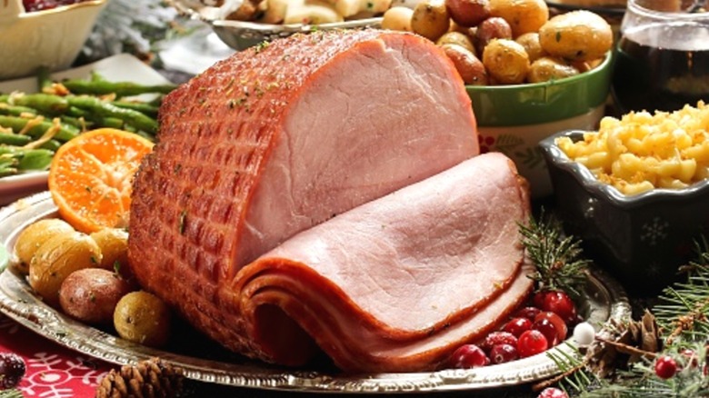 A baked ham on a silver platter with mac and cheese, potatoes, and cranberries