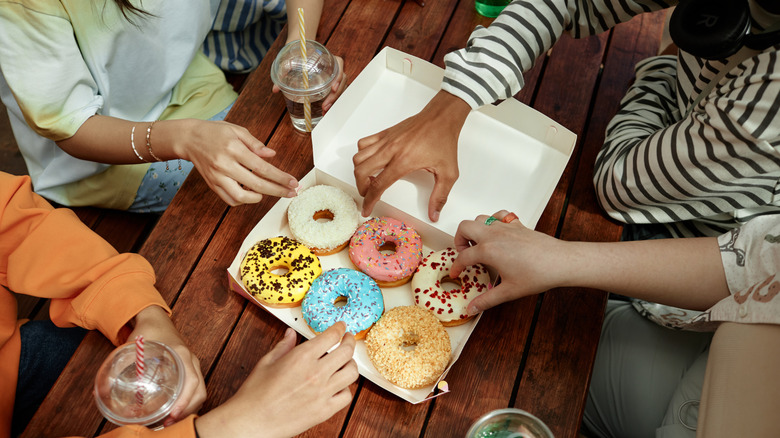 Friends eating colorful donuts at a wood table