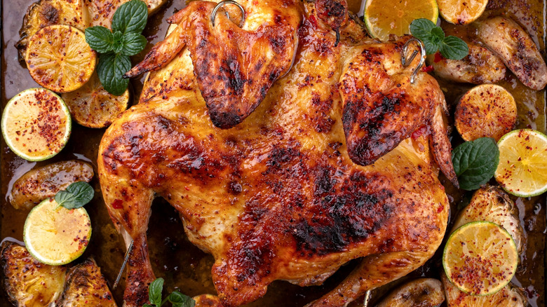Whole roasted chicken on a baking sheet with lemons, pineapples, potatoes, and fresh mint