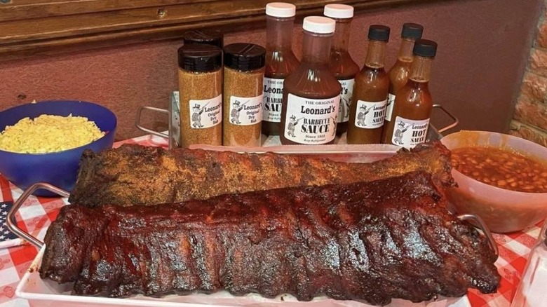 Racks of sauced and dry-rubbed ribs with beans and potato salad pictured with Leonard's BBQ sauce in the restaurant