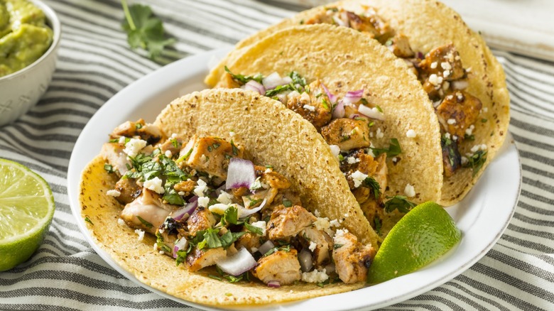 A plate of chicken tacos with lime wedges.