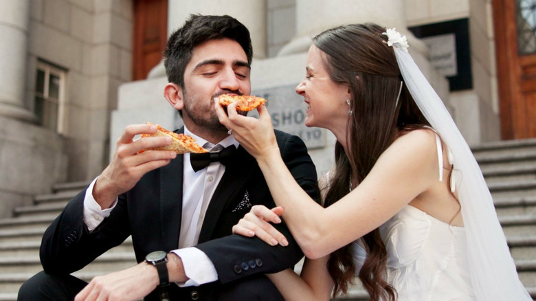 Newlywed man and wife smiling and eating pizza