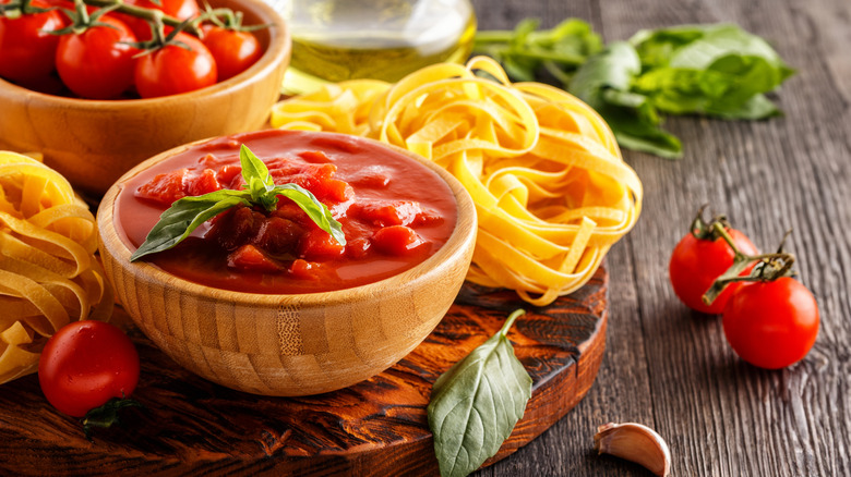 Tomato sauce in a small bowl surrounded by pasta, tomatoes, basil, garlic, and oil.