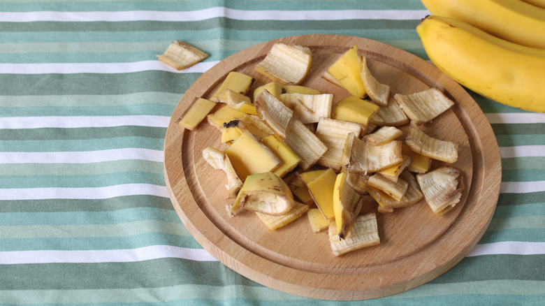Cut up banana peels on a wooden serving board on top of a cloth
