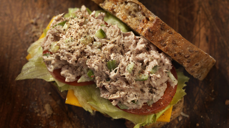 A closeup of an open tuna sandwich on multigrain bread with tomato, lettuce, and cheese