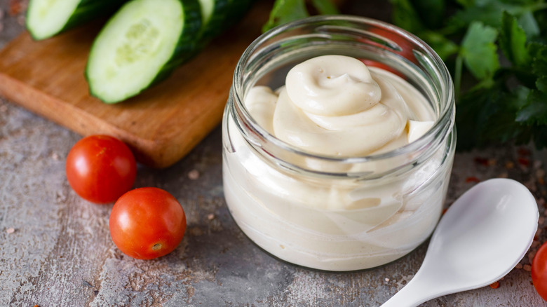 A jar of mayonnaise next to tomatoes and a sliced cucumber