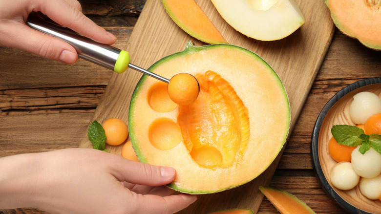 hand uses melon baller tool on cut cantaloupe