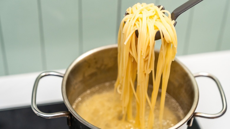 Long spaghetti strands being pulled from pasta water.