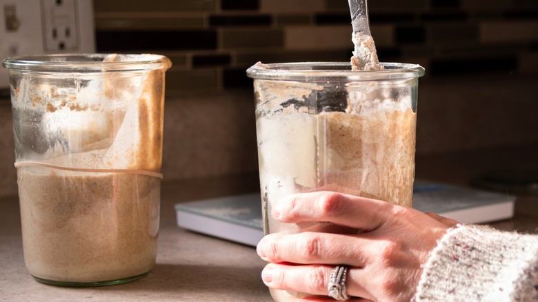 Person in home kitchen stirring sourdough starter with discard off to the side