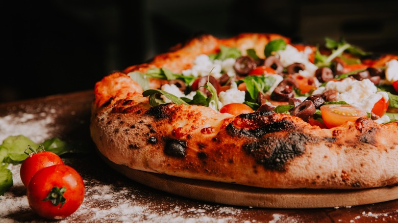 Sourdough pizza topped with cheese, basil, tomatoes, and olives on pizza stone