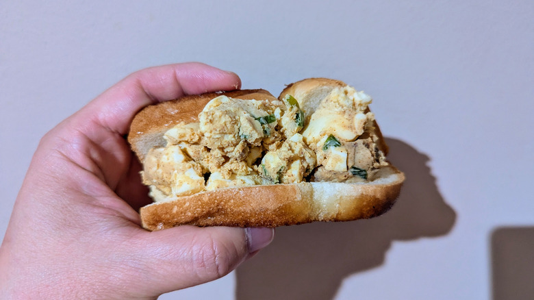 Hand holding egg salad sandwich in single piece of fried white bread.