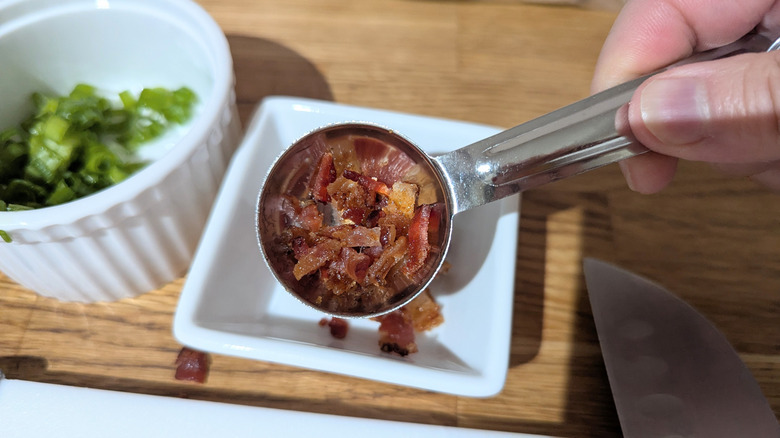 Hand holding tablespoon with bacon in it.