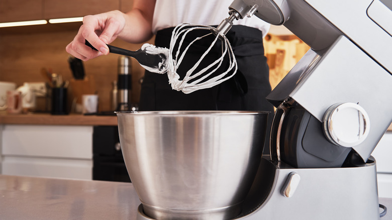 person using tool to scrape whisk on standing mixer