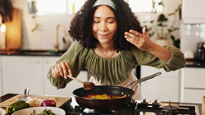 woman smelling the food she is cooking over the stove