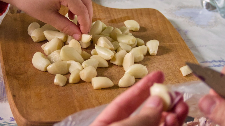 people peeling garlic cloves and placing on a wooden cutting board