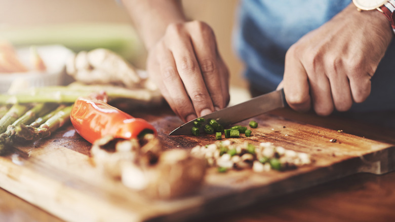 person using knife to cut vegetables on a wooden chopping board