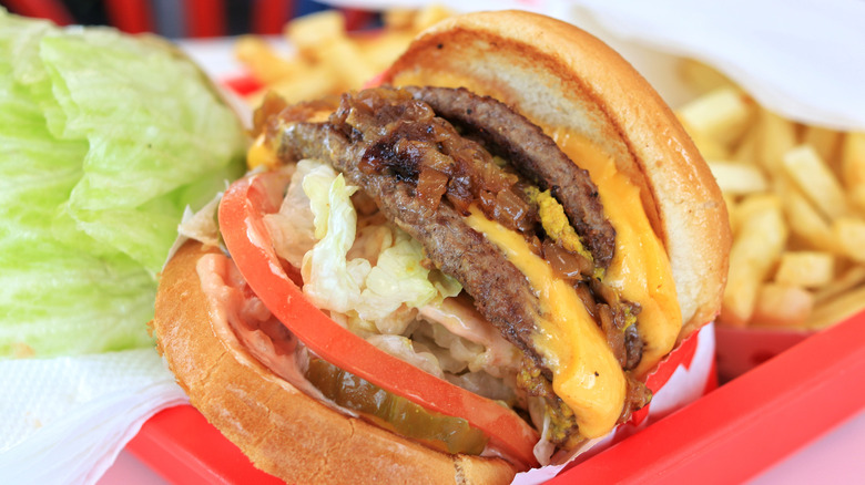 An animal-style cheeseburger from In-N-Out next to fries in red tray