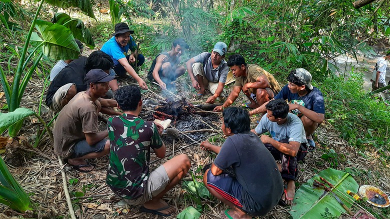 group of people grilling meat over a fire in a jungle