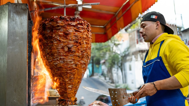 street food vendor preparing to slice hanging meat in a booth