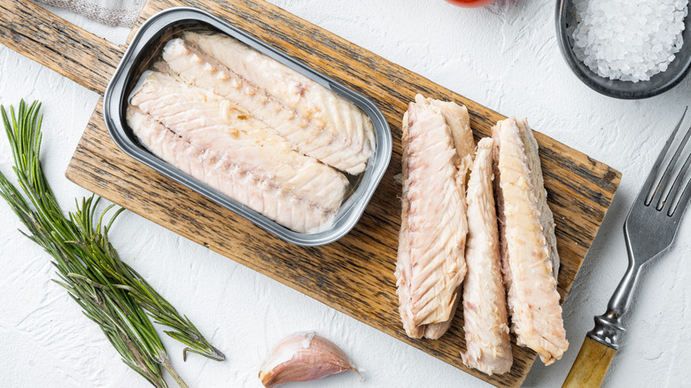 Canned mackerel filets, some inside the can, some removed, on a wooden board