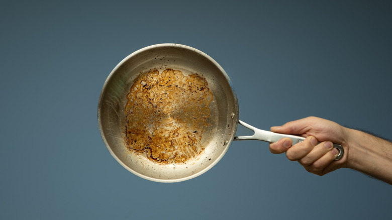 Dirty oily burnt metal frying pan held in hand by a hand