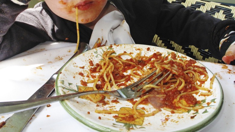 Child messily eating spaghetti in restaurant