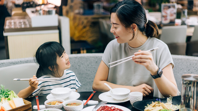 Parent and child holding chopsticks while dining at Asian restaurant