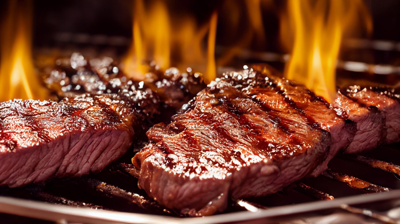 Two steaks being grilled over flames