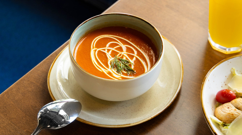 A bowl of tomato soup on a table next to a tall glass of orange juice