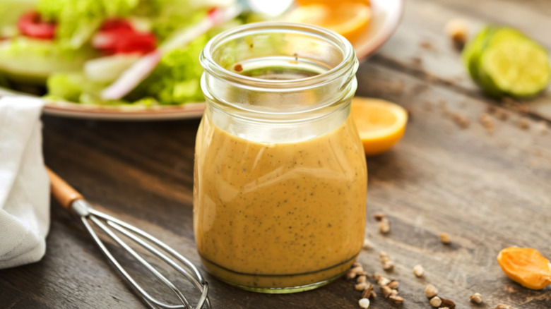 jar of yellow colored dressing with salad in background