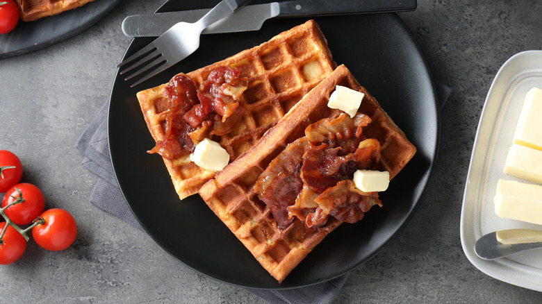 Two waffles with bacon on black plate