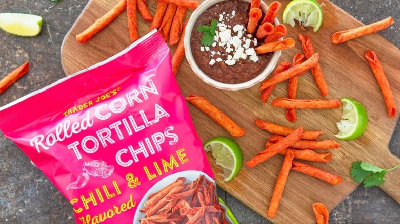 Trader Joe's Chili & Lime Flavored Rolled Corn Tortilla Chips on a wooden board with a bowl of dip and some lime wedges