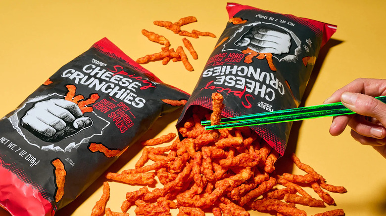 Spilled bags of Trader Joe's Spicy Cheese Crunchies and hand holding green chopsticks