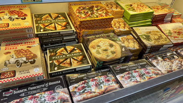 Stacked boxes of Trader Joe's pizzas in a grocery store freezer aisle.