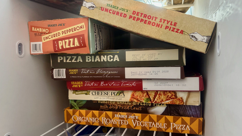 Ten cardboard boxes of different Trader Joe's pizzas stacked on a freezer shelf.