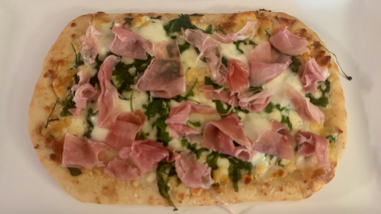 A rectangular pizza topped with green arugula and shaved prosciutto.