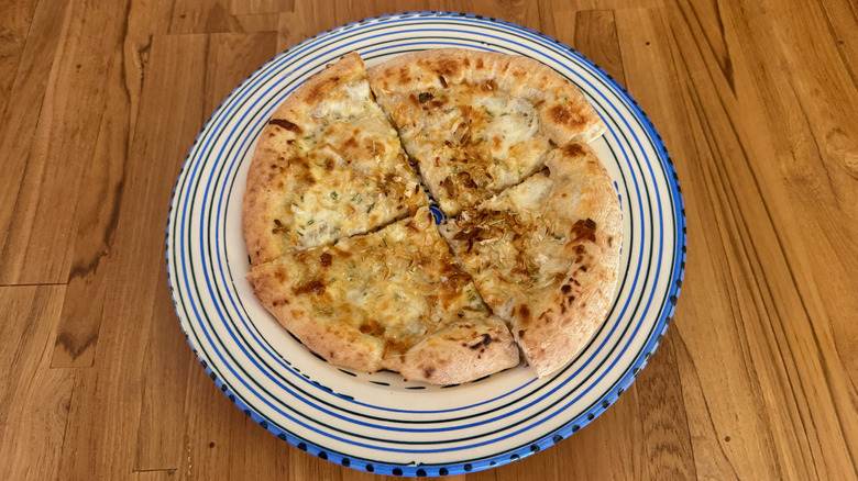 A pizza with a thick, blistered crust and caramelized onions on a blue and white circular serving platter on a wooden table.